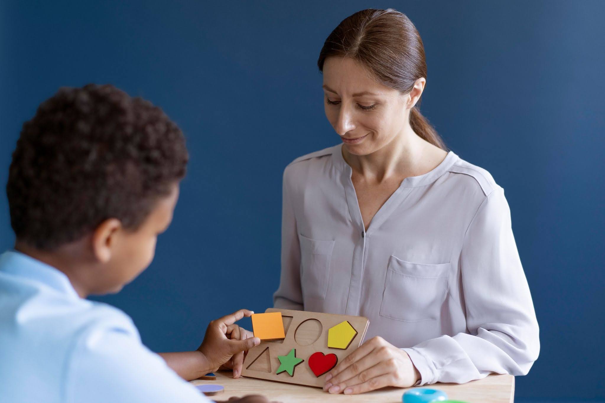 A boy playing a shape game while a woman watches.