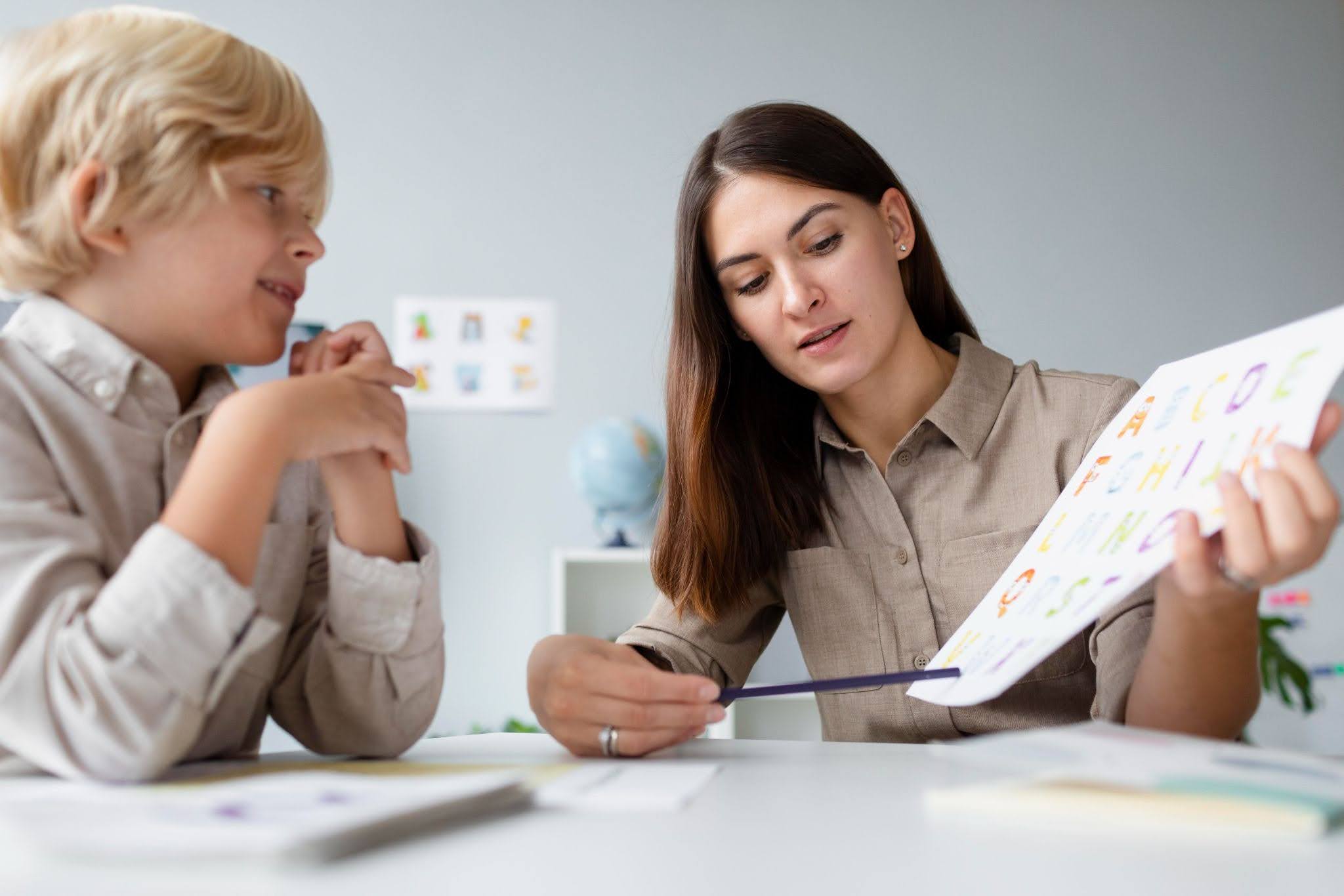 A blond boy being taught the alphabet by a female teacher.