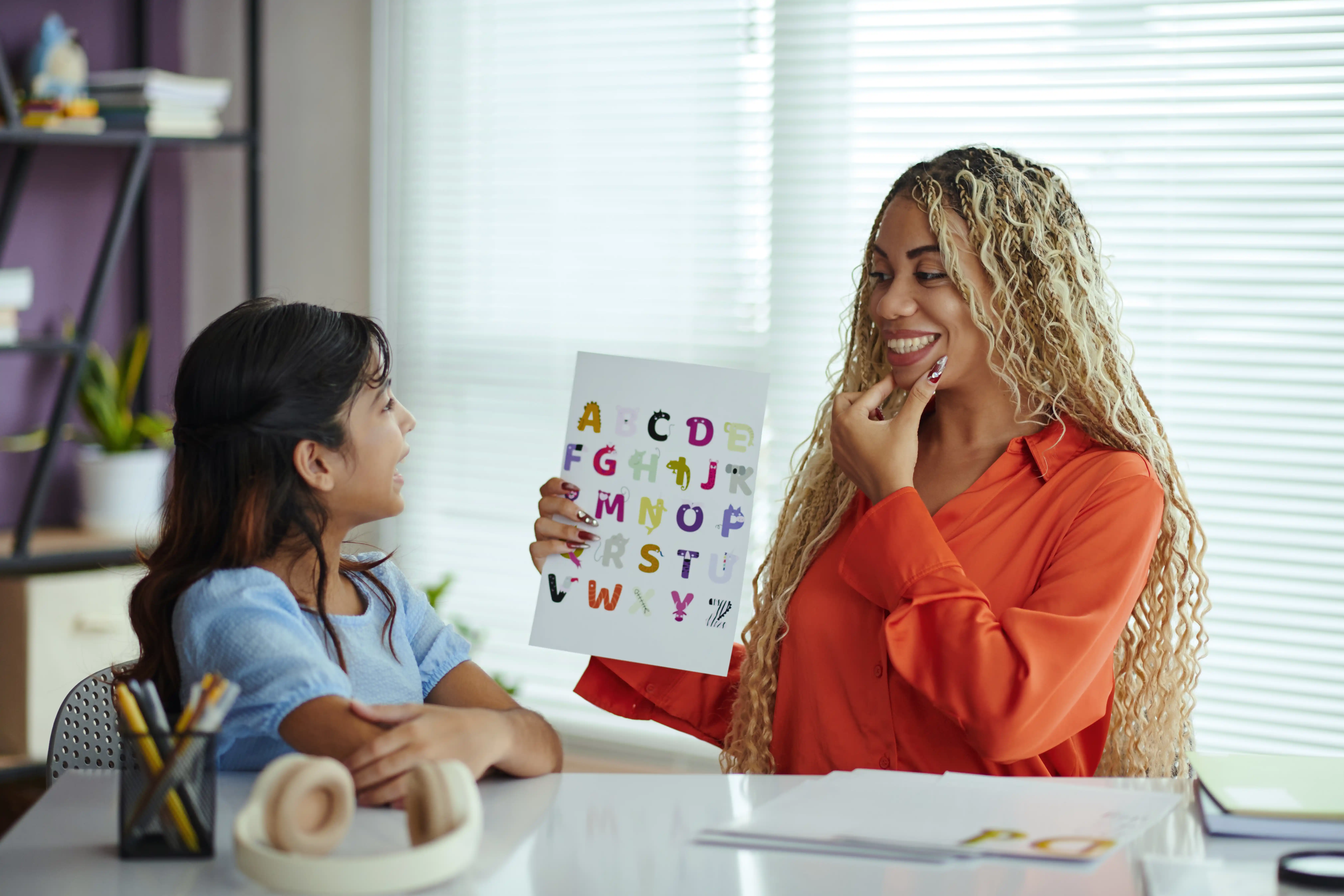 A therapist holding an alphabet chart while sitting with a young child at a table.